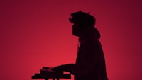 a silhouette of a man playing a keyboard in front of a red light